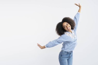 Pozitif, otantik, kıvırcık saçlı, el ele gezen, beyaz arka planda izole edilmiş uçan hareketler yapan, sıradan tişörtlü Afro-Amerikan kadının portresi.