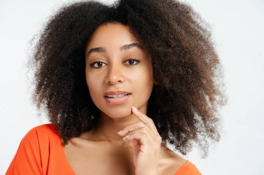 Güzel Afro-Amerikan kadın portresi. Kıvırcık saçlı, kameraya bakıyor ve beyaz arka planda izole bir şekilde poz veriyor. Yakın plan. Cilt bakımı kavramı