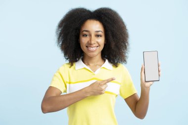 Güzel gülümseyen Afro-Amerikan kadın cep telefonunu göstererek mavi arka planda izole edilmiş bir şekilde işaret ediyor. Modern mobil uygulama kullanan bir kadın. Satış, online alışveriş, siber pazartesi.