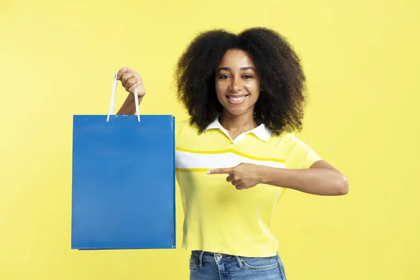 Sarı Arka Planda Mavi Alışveriş Çantası Tutan Güzel Gülümseyen Afro — Stok fotoğraf