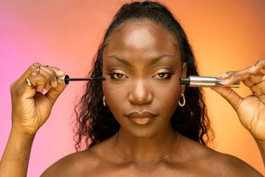 Güzel bir bayanın maskara kullanırken önünde durduğu, renkli arka planda izole bir şekilde. Güzellik, kozmetik konsepti.