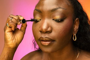 Afrika kökenli Amerikalı kadının rimel tutarken ve sürerken yakın plan çekimleri. Renkli arka plan izole edilmiş. Güzellik, kozmetik konsepti.