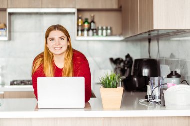 Çekici vücut pozitifliği olan kadın ayakta duruyor, dizüstü bilgisayar kullanıyor modern bir dairede, evinde, mutfakta çalışıyor. Uzak görev kavramı