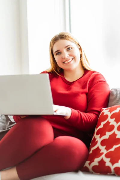 Evdeki modern dairede rahat bir kanepeye oturmuş kameraya bakan güzel, beyaz, sarışın bir kadının portresi. Uzak görev kavramı