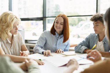 Genç gülümseyen öğretmen ya da öğretmen asistanlık yapıyor, bir şeyleri açıklıyor, dil öğreniyor, ders alıyor, sınıfta zeki gençlerle ders çalışıyor. Eğitim kavramı