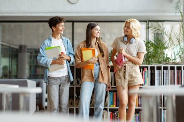 Bir grup zeki gülümseyen üniversite öğrencisi kitap okuyor, konuşuyor, iletişim kuruyor ve modern kütüphanede birbirlerine bakıyorlar. Eğitim kavramı 