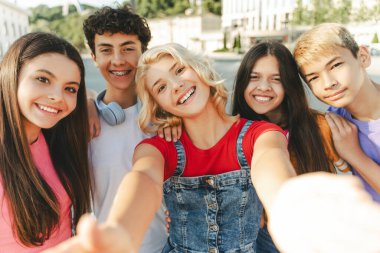 Bir grup gülümseyen arkadaş, çok ırklı gençler selfie çekiyorlar ve sokak kameralarına bakıyorlar. Genç mutlu blogcu etkileyicisi arkadaşlarıyla birlikte video kaydediyor. Yaz konsepti