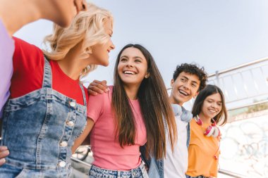 Bir grup gülümseyen arkadaş, renkli kıyafetler giyen, konuşan, sokaklarda yürüyen çok kültürlü gençler. Açık havada mutlu stil sahibi kızlar ve erkekler. Arkadaşlık, pozitif yaşam tarzı, çeşitlilik 