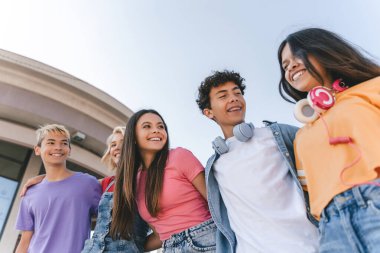 Bir grup gülümseyen arkadaş, renkli kıyafetler giyen, konuşan, sokaklarda yürüyen çok kültürlü gençler. Açık havada mutlu stil sahibi kızlar ve erkekler. Arkadaşlık, pozitif yaşam tarzı, çeşitlilik 