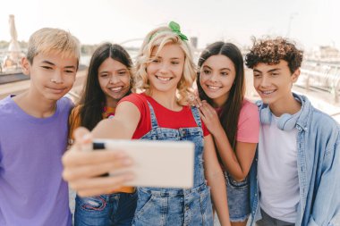 Sokakta selfie çeken, gülümseyen çok kültürlü gençlerden oluşan bir grup. Genç mutlu blogcu etkileyicisi arkadaşlarıyla birlikte video kaydediyor. Teknoloji. Yaz, pozitif yaşam tarzı konsepti 