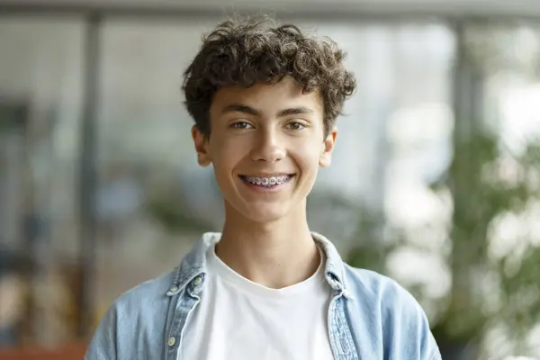 スマートなカーリーハイレッドの学校の少年がカメラを見ている歯のブレースを着用する微笑みを閉じる肖像画 教育コンセプト — ストック写真