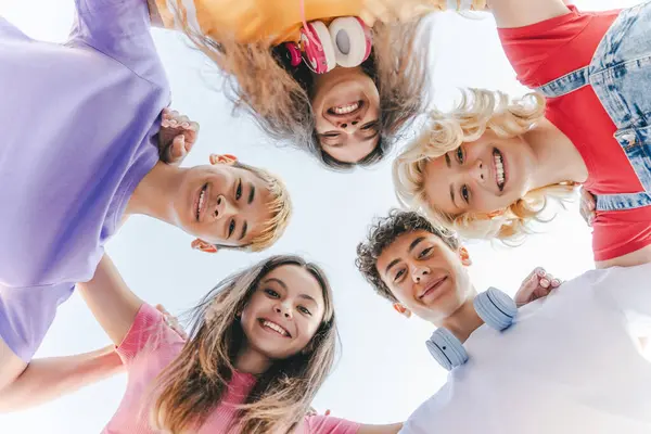 Renkli tişörtler giyen, kucaklaşan, caddede kameraya bakan çok kültürlü arkadaşların portresi. Mutlu okul kızları ve oğlanlar çember oluşturuyorlar. Tatil, yaz, arkadaşlık. 