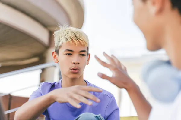 Portrait of pensive attractive Korean boy with colored hair, talking, gesturing. Stylish young hipster man wearing casual clothes on street meeting with friends. Concept of friendship, communication