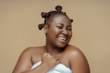 Afro-gülümseyen Afro-Amerikan kadın portresi havluyla dikilip aynaya bakıyor kahverengi arka planda. Çekici artı mohel stüdyoda fotoğraf için poz veriyor.