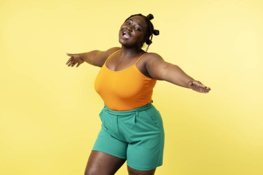 Güzel, çekici, iri yarı, sarı arka planda dans eden gündelik kıyafetler giyen Afrikalı bir kadın. Vücut pozitifliği olan bir kadın eğleniyor. Pozitif yaşam tarzı