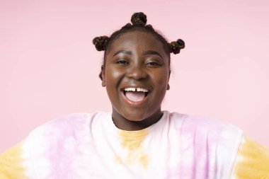 Yakın plan, pembe arka planda izole edilmiş kameraya bakan, günlük tişört giyen, gülümseyen Afrikalı bir kadının portresi. Resim için güzel artı boyut modeli