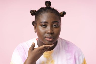 Pembe arka planda izole edilmiş tişört giyen düşünceli Afrikalı güzel bir kadının portresi. Görüntü için poz veren pozitif vücut modeli kameraya bakıyor.
