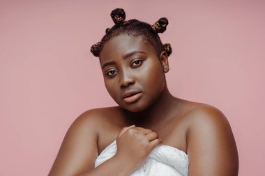 Havluyla poz veren güzel ve büyük model. Pembe arka planda izole edilmiş kameraya bakıyor. Güzellik prosedürleri kavramı, hijyen kavramı