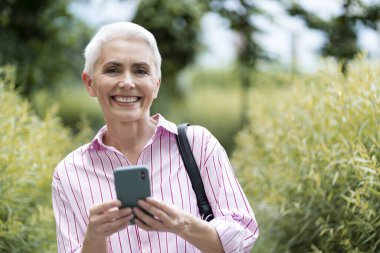 Gülümseyen ve elinde cep telefonu olan olgun bir kadın sokakta alışveriş yapıyor, fotokopi çekiyor. Çekici, kır saçlı, yaşlı kadın mektupları kontrol ediyor. Teknoloji konsepti