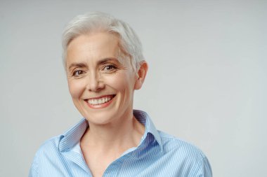 Caucasian gray haired senior woman smiling broadly looking at camera, isolated on grey background. Close-up studio portrait of mature adult female pensioner, expressing positive emotions  clipart