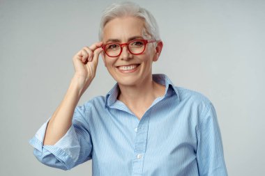 Gri arka planda izole edilmiş kırmızı gözlük takan gülümseyen son sınıf öğrencisinin orijinal portresi. Çekici, mutlu, gri saçlı iş kadını, kendine güvenen yönetici kameraya bakıyor. 