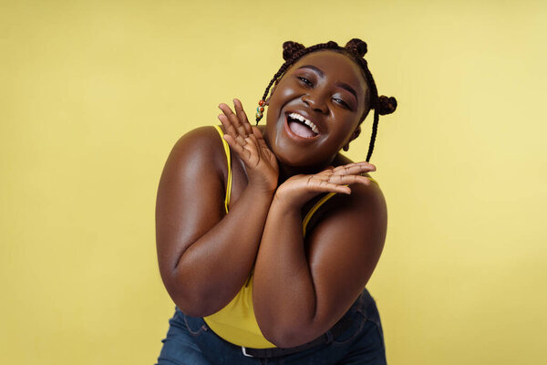 Attractive young african american woman smiling touching face posing for picture on yellow background. Beautiful female with stylish hairstyle, beauty concept