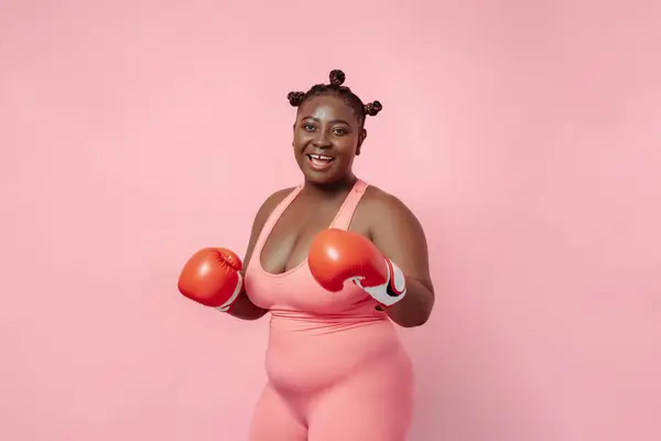 Stock image Portrait of body positive African woman wearing red boxing gloves isolated on pink background. Female training, motivation, hobby