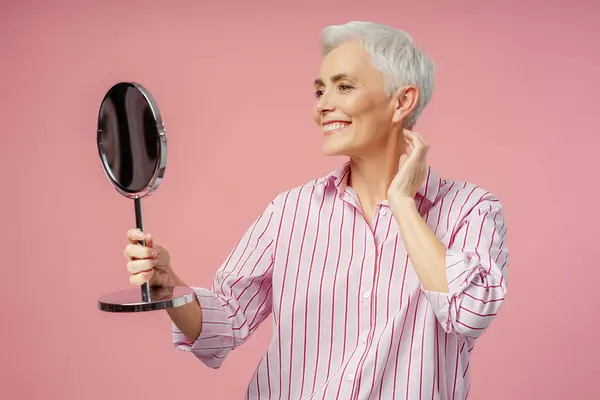 Улыбающаяся Пожилая Женщина Седыми Волосами Стильный Макияж Выглядящий Зеркале Розовом — стоковое фото