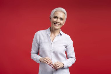 Gündelik tişört giyen, elinde gözlük tutan ve kameraya bakan kendine güvenen bir bayan öğretmen. Başarılı iş kadını kırmızı leylak arka planda izole edildi, boşluğu kopyala