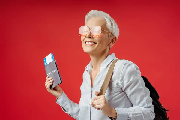 Счастливая Позитивная Пожилая Женщина Рюкзаком Держащая Паспорт Билеты Красном Фоне — стоковое фото