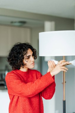 Kıvırcık orta doğulu kadın evde yüksek kaliteli ışıklandırma elde etmek için yanan ampulü kendi başına değiştiriyor. Gülümseyen kız avizeye ampul yerleştiriyor.