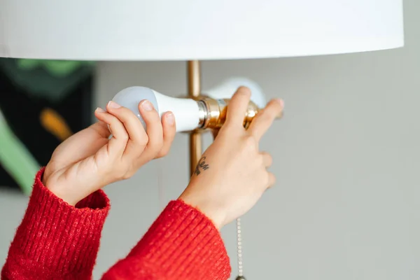 Close up view of woman inserts light bulb into chandelier at home. Girl independently changes burned-out light bulb in order to achieve high-quality lighting in house