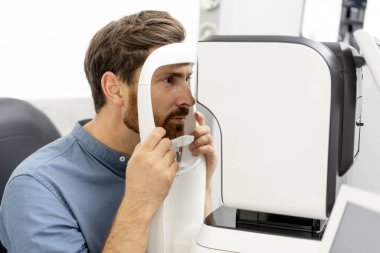 Genç adam optik mağazasında otomatik fraktör ile görüşü kontrol ediyor. Sağlık, ilaç, insan konsepti