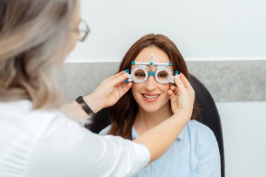 Kadın optometrist göz kliniğinde gülümseyen kadın görüşünü kontrol ediyor. Sağlık, ilaç, insan konsepti