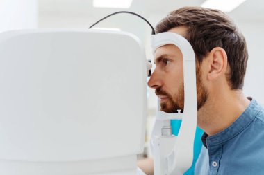 Göz doktorunun dolabında oturan yakışıklı adam gözlerini kontrol ettiriyor. Teşhis konsepti