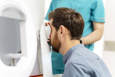 Göz kliniğindeki erkek hasta görüşünü kontrol eden otomatik fraktörlü bir optometrist. Teşhis, sağlık hizmeti kavramı