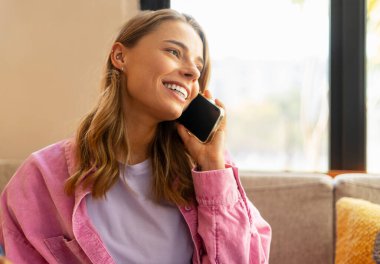 Gülümseyen, cep telefonu tutan, konuşan, telefonlara cevap veren oturma odasındaki kanepede oturan güzel bir kadın. İletişim konsepti