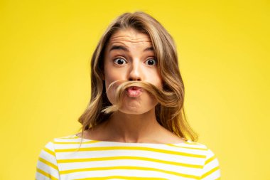 Saçlarıyla oynayan çekici genç bir kadının portresi, somurtkan bakışlarını sarı arka planda soyutlanmış bir şekilde gösteriyor. Olumlu yaşam tarzı kavramı