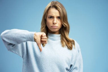 Mavi arka planda izole edilmiş kameraya bakmaktan hoşlanmayan üzgün bir kadının portresi. Reklam kavramı