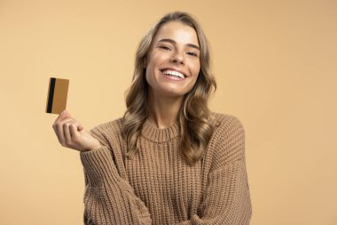 Elinde altın kredi kartıyla bej arka planda izole edilmiş kameraya bakan çekici bir kadının portresi. Alışveriş, tasarruf, banka konsepti 