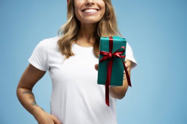 Gülümseyen güzel bir kadın elinde kırmızı kurdeleyle mavi arka planda duran bir hediye kutusu, seçici bir odak noktası var. Tatil, doğum günü kutlaması konsepti