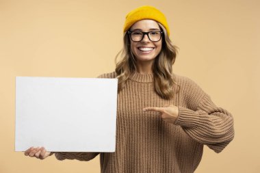 Sarı hippi şapkalı, şık gözlüklü, genç ve mutlu bir kadın. Arka planda izole edilmiş fotokopi alanını gösteren boş bir poster. Pankartla gülümseyen zeki bir öğrencinin portresi 