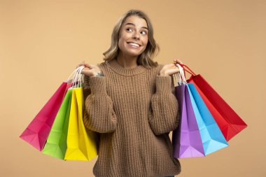 Renkli alışveriş torbaları tutan sevimli bir kadın bej arka planda izole edilmiş bir şeyi seçiyor. Alışveriş, satış, siber pazartesi konsepti 