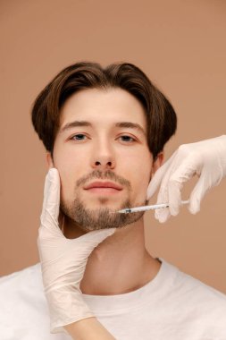 Genç bir adamın yaşlanmayı önleme prosedürünü yakından takip edin. Bej arka planda izole edilmiş. Güzellik bakımı, yaşlanma karşıtı prosedürler, estetik ameliyat konsepti.