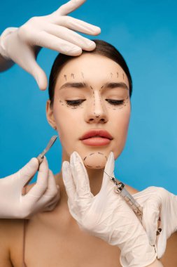 Mavi arka planda, yaşlanma karşıtı operasyona hazır güzel bir genç kadının portresi. Doktor, estetik cerrah hastanın çenesine gençleştirme tedavisi uyguluyor. Kozmetoloji, yüz gerdirme