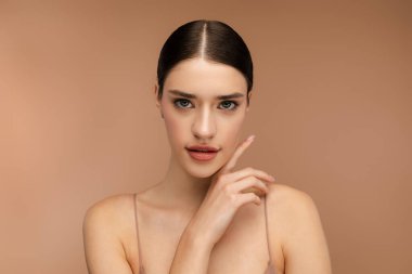 Kameraya bakan doğal makyajlı neşeli bir bayan portresi. Bej arka planda izole edilmiş. Cilt bakımı, güzellik prosedürü, sabah rutini kavramı