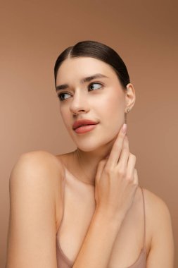 Stüdyoya bakan güzel bir kadının portresi. Doğal makyajlı, şık bir saç stili. Bej arka planda izole edilmiş. Cilt bakımı, güzellik prosedürü, sabah rutini
