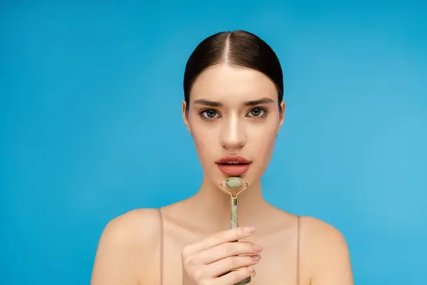 stock image Close up of beautiful woman holding stone facial roller while massaging her chin. Isolated on blue background. Skin care, anti aging procedure