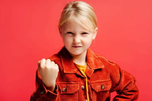 愤怒的小女孩穿着时髦的休闲棕色夹克 露出拳头 看着被红色背景隔离的相机 情绪的概念 — 图库照片