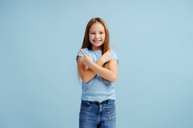 Şık giyinmiş, şık giyinmiş, fotokopi alanını gösteren ve mavi arka planda izole edilmiş kameraya bakan güzel bir kızın portresi. Reklam kavramı